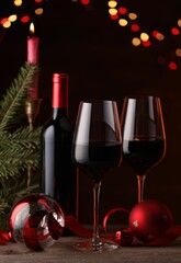Red wine, Christmas ornaments and fir branch on wooden table against blurred festive lights