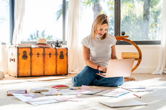 Female working at home with laptop surrounded by papers