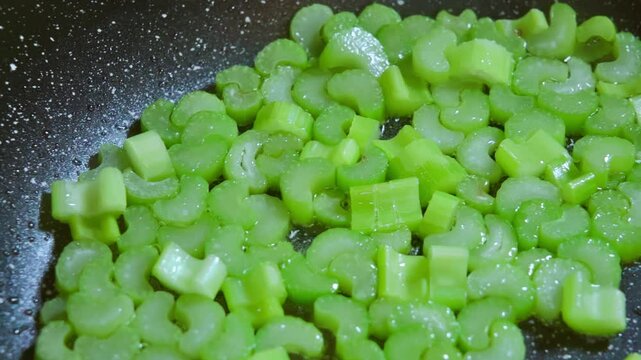 Chopped celery stalks are fried in a pan in hot olive oil. Frying celery stalks. Healthy eating concept.