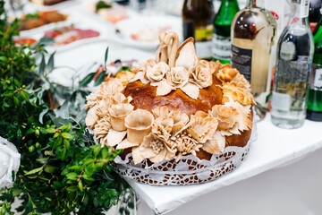 loaf decorated with complex dough patterns. On the top of the loaf there are two figures of swans, and around them there are flowers and leaves, also made from dough.