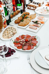 festive table with various dishes and drinks. In the foreground there is a plate with sliced ​​sausage and meat