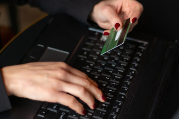 Businesswoman shopping online with a credit card at a table. Hand holding a card and typing on a laptop keyboard. E-commerce concept with shopping cart
