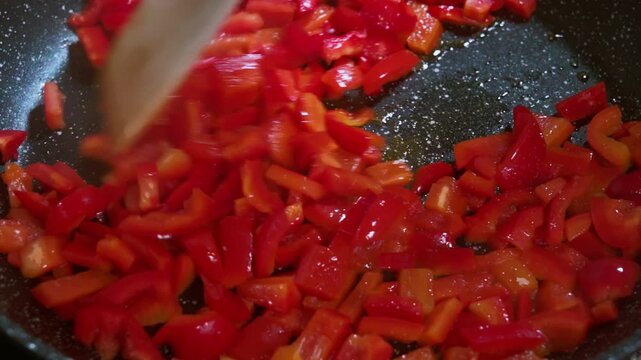 Chopped red bell pepper in a frying pan are fried and stirred with a wooden spatula. Close-up Cooking Process, Healthy Food, Vegetarian Cuisine Vegetarian Organic Health Food. Slow motion video.