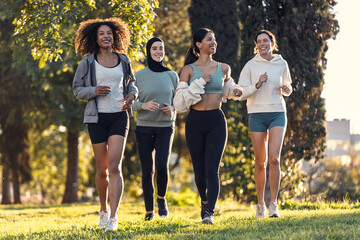 A group of four sportswomen running together through the park
