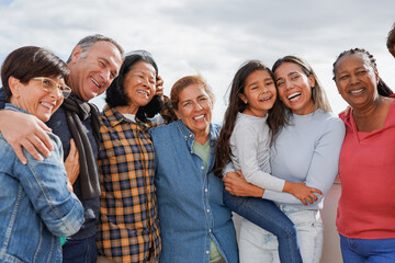 Group of multi generational people hugging each other while smiling in front of camera - Multiracial friends having fun together outdoor