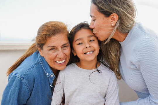 Multi generational family smiling in front of camera - Mother kissing little daughter outdoor