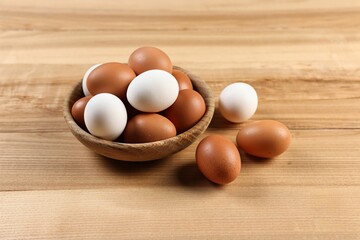 Raw eggs in bowl on wooden table, closeup