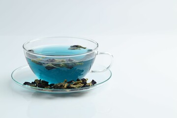 Fresh butterfly pea flower tea in cup and dry petals on white table, closeup. Space for text