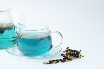 Fresh butterfly pea flower tea in cup, teapot and dry petals on white table, closeup. Space for text