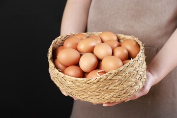 Woman with basket of eggs on black background, closeup