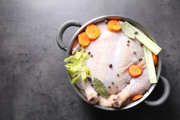 Whole raw turkey, cut carrot, celery and spices in pot on grey textured table, top view. Space for text