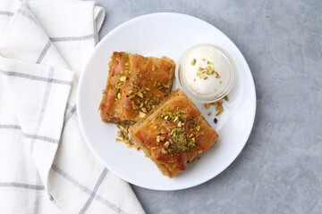 Tasty baklava with chopped nuts and scoop of ice cream on grey table, top view