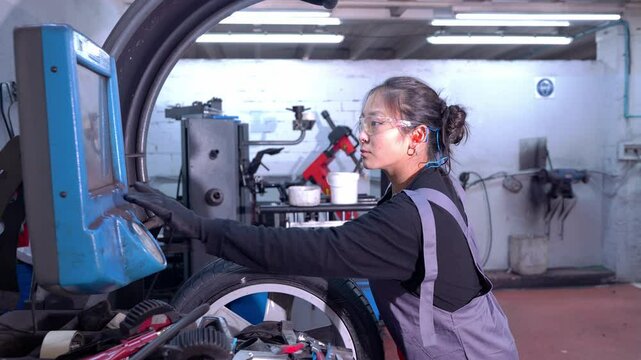 Skilled female mechanic operating tire balancing machine in a professional car repair shop