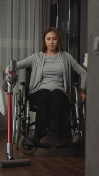 Woman with paralysis removes dust in house using convenient device. Young woman with injury uses medical equipment to move while doing household chores