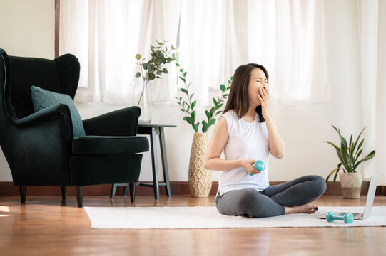 Asian woman yawning tired covering mouth with hand while trying to do exercise in living room at home. restless and sleepiness.