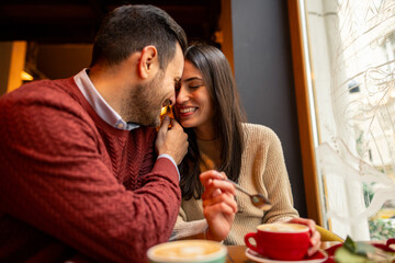 A Caucasian mid adult couple enjoys International Women's Day at a cozy cafe. They share light conversation over coffee and dessert. Their smiles radiate warmth and joy.