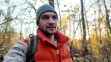 A young male blogger walks through autumn forest and shoots videos using a phone or action camera. A traveler guy takes a selfie and talking while filming a vlog outdoor. Solo travel concept