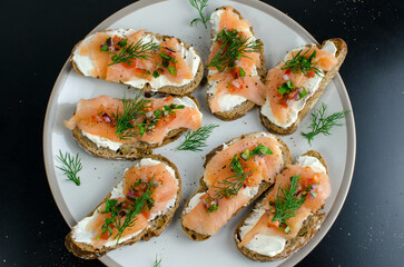 Smoked Salmon bruschetta with soft cheese spread, fresh tomato salsa and homemade bread, on a plate on a black table