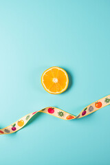 A small orange slice is placed on a large blue background next to a ribbon with colorful fruit patterns printed on it._00002_