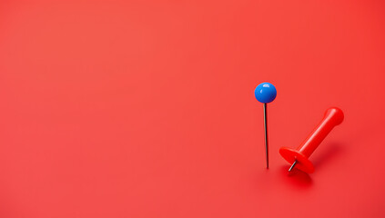 A small group of a pin and thumbtack sits on a red desk with plenty of space for text overlay._00003_