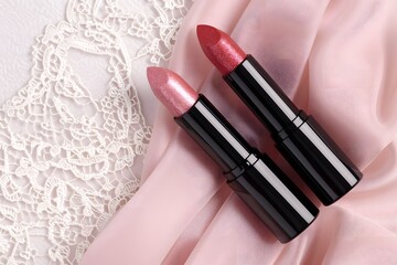 Obraz premium Two pink lipsticks on delicate lace and satin fabric background. Feminine beauty flat lay composition for makeup and cosmetic branding.