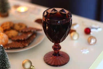 Various Christmas decorations, cookies, chocolate, nuts and tangerines, wine glasses and lit candles on the table. Holiday hygge at home. Selective focus.