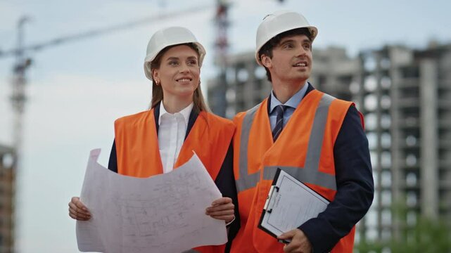Smiling builders review construction plans at outdoor building site closeup.