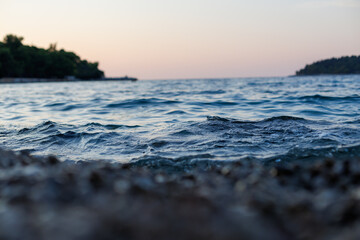 Obraz premium Waves gently lapping on the shore at sunset along a serene coastal landscape with distant islands and a colorful sky