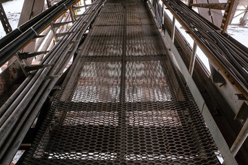 Expanded metal steel floor of busbar gallery. Сable ducts on a pass-through cable overpass. Industrial conduit corridor.