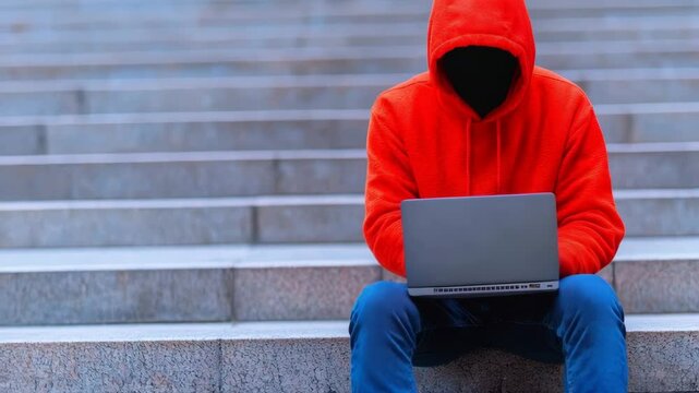 Analyze the techniques of overpayment scams targeting freelancers and small businesses, A hooded figure using a laptop on stairs