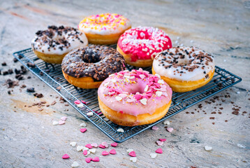 Traditional festive glazed doughnuts with icing sugar and chocolate decorated with colorful coatings and sprinkles on a cooking rack