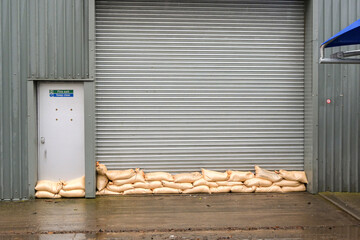 Sandbags stacked against the roller door of a factory to prevent flooding from  floodwater after...