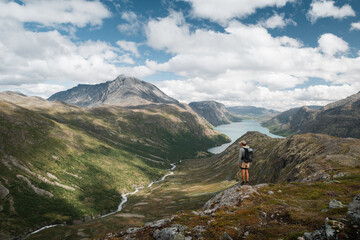 Trekker admiring Norway's Jotunheimen mountains and winding river.