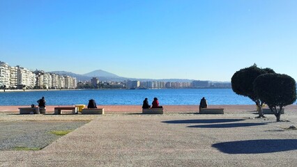 Photo of people sitting on the promenade of the old port and enjoying the breathtaking views of Thessaloniki's waterfront and the thermaic gulf.