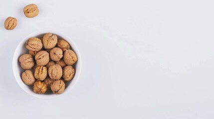 Bowl of unshelled walnuts with a few scattered on a white background, flat lay nut photography, healthy snack concept, natural ingredient design with copy space for text.

