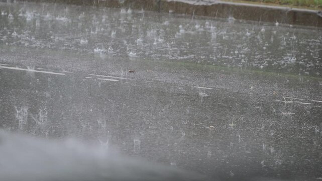 Surface of asphalt road covered with water with traces of falling raindrops during heavy rain in city. Background video of bad weather and flowing streams of water on city street.