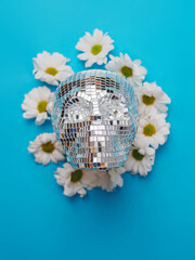 A party skull is surrounded by white flowers. The skull is made of small mirrors. The flowers are arranged around the skull in a way that creates a sense of balance and harmony