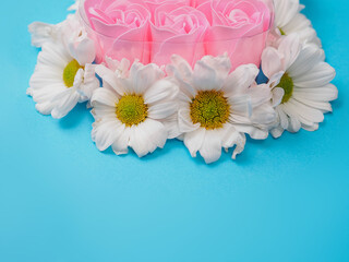 Obraz premium A heart made of six pink roses. The roses are surrounded by white daisies places on blue color simple background. Concept of love and affection. Abstract conceptual art.