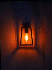 A lamp is lit up and casting a warm glow on the wall creating sense of comfort. The light is yellow and the lamp is sitting on a wall