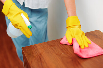 Woman in yellow rubber gloves cleaning wooden table with rag and cleaning solution bottle