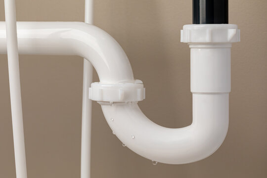Water dripping from leak on sink drain trap pipes. Plumbing repair and home maintenance concept.