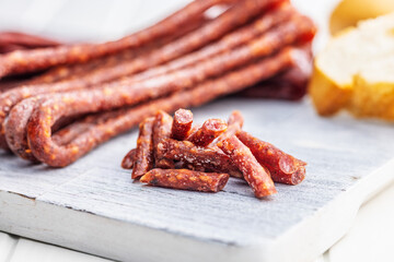 Smoked kabanos. Mini dried thin sausages on cutting board on white table.