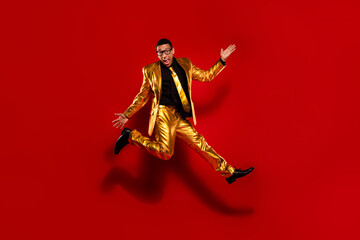 Energetic young man in a stylish gold suit jumping against a vibrant red background, exuding charm...