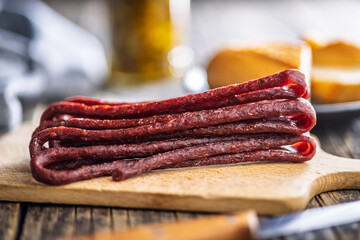 Smoked kabanos. Mini dried thin sausages on cutting board on wooden table.