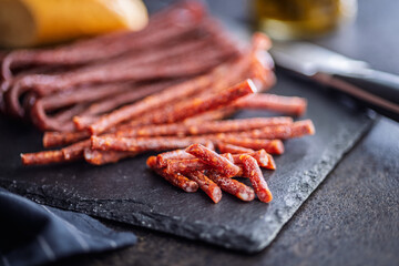 Smoked kabanos. Mini dried thin sausages on cutting board on black table.
