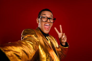 Young man in a golden suit making a peace sign with a vibrant red background, exuding confidence...