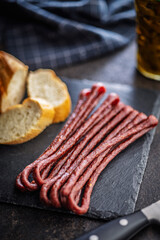Smoked kabanos. Mini dried thin sausages on cutting board on black table.