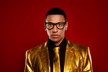 Young man in a glossy golden suit stands confidently against a red background, embodying elegance and modern style.
