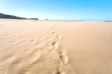 Sand dunes with human footprints near seaside. Hot sunny day in deserted place