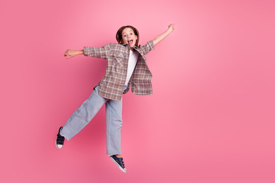 Cheerful young girl jumping against a pink background wearing a checkered shirt and casual stylish outfit